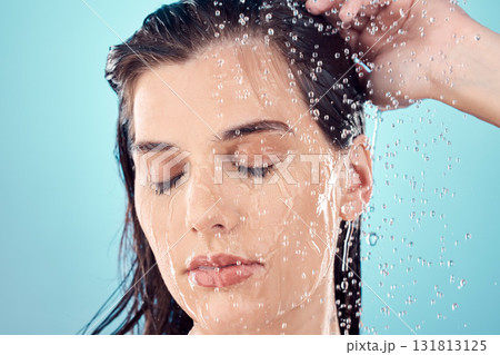 Water splash, hair care and face of woman in shower in studio isolated on a blue background. Beauty, eyes closed and young female model washing, cleaning or bathing for hygiene, skincare and health. 131813125