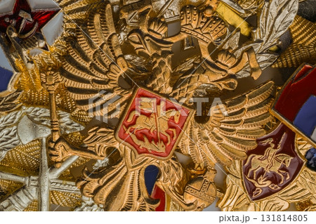 Macro stack including two gold Russian Soviet military gold double headed eagle and coat of arms medal with red field. Russian Federation flag pin. Ruby star hero of nation. Closeup macro flat lay Macro stack including two gold Russian Soviet military gold double headed eagle and coat of arms medal with red field. Russian Federation flag pin. Ruby star hero of nation. Closeup macro flat lay 131814805