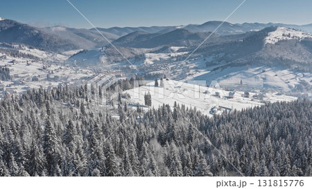 Capturing breathtaking aerial views of a picturesque village nestled among snow-covered hills and vast pine forests, creating a serene winter wonderland in the Carpathian Mountains. Bukovel ski resort 131815776