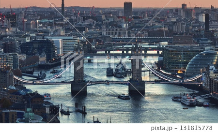 Aerial view of Tower Bridge and HMS Belfast warship on River Thames at sunset, with London skyline cityscape in background, offering a captivating urban landscape. Travel to UK. Drone flight 131815778