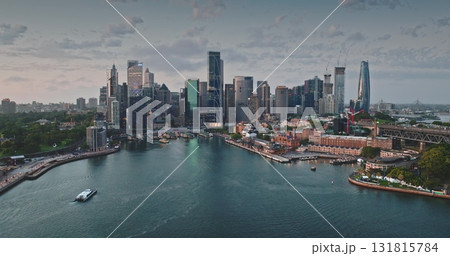 Australia, Sydney: Breathtaking aerial view of Sydney modern skyline city center reflecting in calm harbor waters. Iconic skyscrapers cityscape illuminated by soft sunset light. Drone panorama 131815784