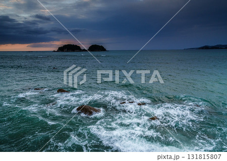 雲間から覗く夕焼けと 岩場に打ち寄せる白波⑪ 131815807
