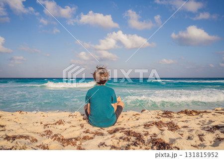 Teenage boy meditating on the sandy beach by the ocean, practicing mindfulness and inner peace during summer vacation. Wellness, balance, healthy lifestyle and tranquility concept. Teenage boy meditating on the sandy beach by the ocean, practicing mindfulness and inner peace during summer vacation. Wellness, balance, healthy lifestyle and tranquility concept. 131815952