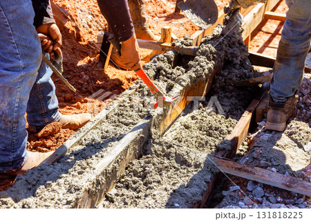 Workers mix pour fresh concrete into wooden forms, preparing foundation under curbed is concrete Workers mix pour fresh concrete into wooden forms, preparing foundation under curbed is concrete 131818225