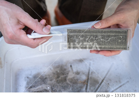Woman using small brush for cleaning vacuum dust filter. Cleaning filter protect the overall air quality in your home as well by capturing dust, debris, and other allergens. 131818375