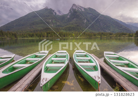 Green rowboats moored to wooden docks on clear mountain lake with forest and peaks in background Green rowboats moored to wooden docks on clear mountain lake with forest and peaks in background 131828623