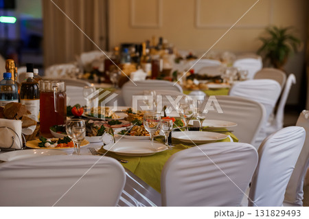 Elegant Banquet Table Setting with Wine, Fine Dining Food, and White Chairs in a Dimly Lit Event Venue. 131829493