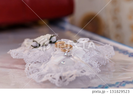 Elegant Wedding Rings on White Pillow, Close-Up Shot, Floral Decoration, Gold Bands, Lace Fabric, Symbolic Love and Commitment, Soft Lighting 131829523