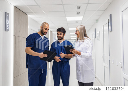 A doctor and two nurses are reviewing medical records in a clinic hallway, discussing patient care. 131832704