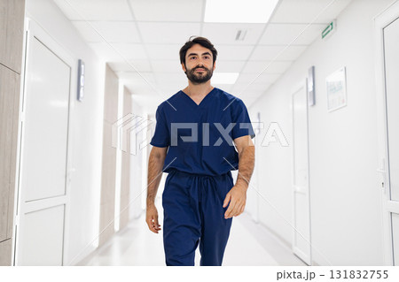 A doctor in scrubs walks confidently down a bright clinic hallway, ready to assist patients. 131832755