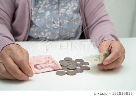 Retired elderly woman counting coins money with piggy bank and worry about monthly expenses and treatment fee payment. 131836813