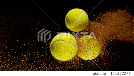 Freeze motion shot of a yellow tennis balls flying through the air, followed by a dynamic trail of clay dust.  131837277