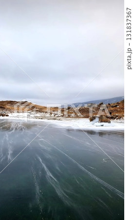 Frozen Lake Baikal shore with smooth ice leading to rocky brown hills 131837367