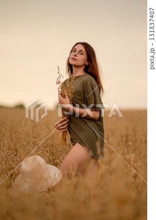 Woman holding wheat while standing in an oat field at sunset Woman holding wheat while standing in an oat field at sunset 131837407