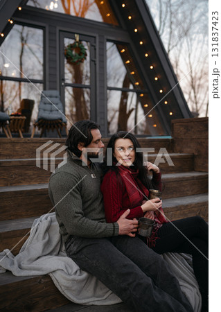 Couple enjoys cozy moments on steps of a modern cabin during winter evening 131837423
