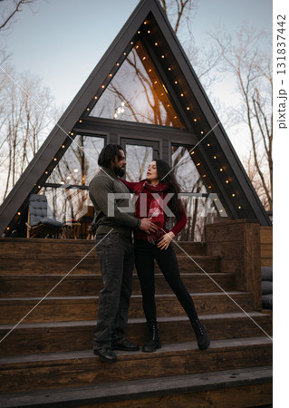 Couple enjoys an intimate moment outside a modern cabin at dusk in the woods Couple enjoys an intimate moment outside a modern cabin at dusk in the woods 131837442