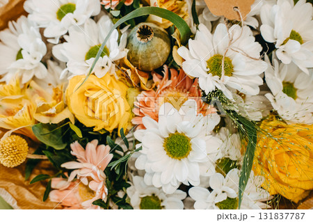 Bright floral arrangement with yellow roses, daisies, and wild accents in a textured Thanksgiving bouquet. Thanksgiving floral decor, bold seasonal color, modern rustic styling, nature-inspired design 131837787