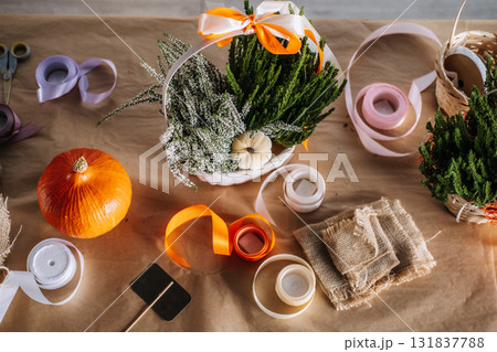 Overhead view of a Thanksgiving floral gift basket with heather, greenery, and ribbon surrounded by crafting supplies. Thanksgiving craft, seasonal floristry, handmade gifting, DIY workshop Overhead view of a Thanksgiving floral gift basket with heather, greenery, and ribbon surrounded by crafting supplies. Thanksgiving craft, seasonal floristry, handmade gifting, DIY workshop 131837788