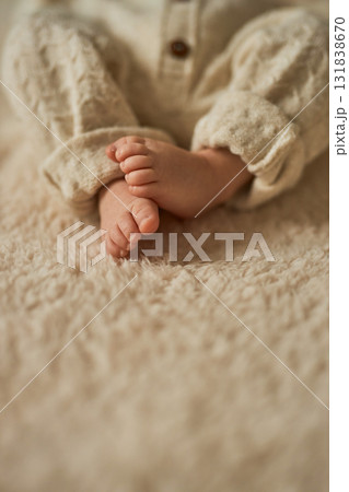 Close-up of a newborn baby's tiny bare feet in a cozy, neutral-toned knit romper, resting on a soft 131838670