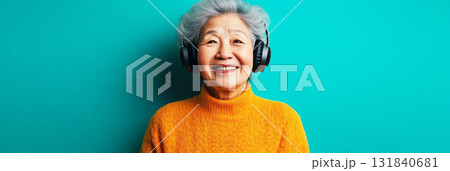 A smiling Asian senior woman with headphones on, basking in the pleasure of listening to music or studying, set against a soft mint background, reflecting the joy and wisdom of old age, banner 131840681