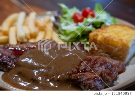 Medium rare meat steak, topped with black pepper sauce on plate with French fries and bread. 131840957