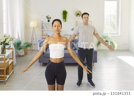 Couple practicing yoga workout and meditation at home, breathing with hands up Couple practicing yoga workout and meditation at home, breathing with hands up 131841351