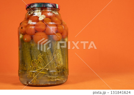 Homemade pickled canned tomatoes and cucumbers in glass jar on orange background 131841624