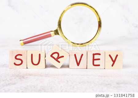 Wooden blocks spell out SURVEY, with one block slightly askew. A gold magnifying glass rests nearby. Analysis and planning concept for improved performance are suggested 131841758