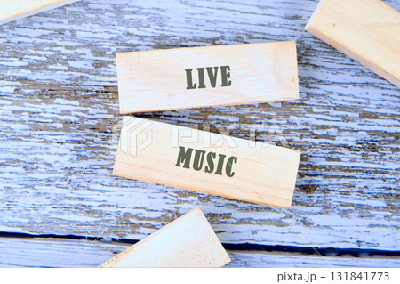 Wooden blocks are arranged on a rustic, painted surface. Two blocks display the words LIVE and MUSIC in a simple, bold font, suggesting a musical performance Wooden blocks are arranged on a rustic, painted surface. Two blocks display the words LIVE and MUSIC in a simple, bold font, suggesting a musical performance 131841773
