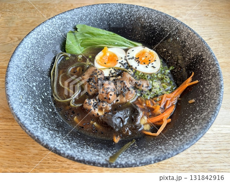 Delicious ramen noodle soup with chicken, boiled egg, and green onions served in a dark ceramic bowl. Traditional Asian Japanese food concept, top view 131842916