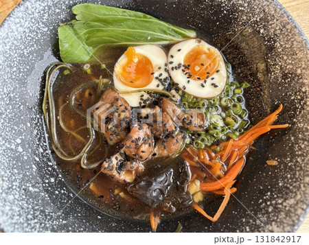 Delicious ramen noodle soup with chicken, boiled egg, and green onions served in a dark ceramic bowl. Traditional Asian Japanese food concept, top view Delicious ramen noodle soup with chicken, boiled egg, and green onions served in a dark ceramic bowl. Traditional Asian Japanese food concept, top view 131842917