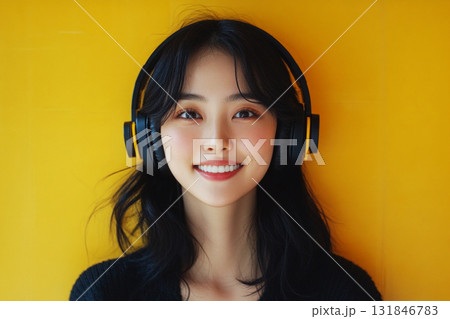 A smiling Asian girl with headphones on her head, set against a yellow background, embodying the pleasure of listening to music or studying in a relaxed and joyful moment A smiling Asian girl with headphones on her head, set against a yellow background, embodying the pleasure of listening to music or studying in a relaxed and joyful moment 131846783