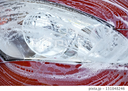 Front head light of red car washed in self serve carwash, white soap strokes on glass 131848246
