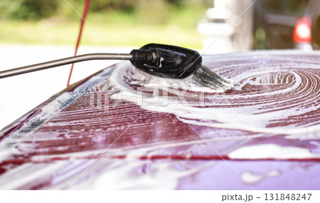 Brush leaving strokes in white shampoo and foam on roof of red car washed in self serve carwash. 131848247
