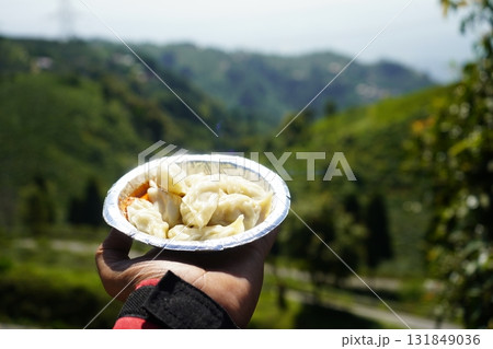 Close up of Steamed Momos Held Against a Blurred Panoramic Green Mountain Landscape 131849036
