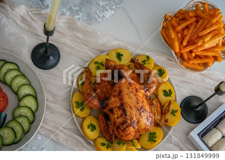 Close-up top view of a festive holiday table featuring a whole roasted chicken, fresh vegetables, and crispy fries. Cozy Christmas, Thanksgiving, or New Year family celebration with colorful and 131849999