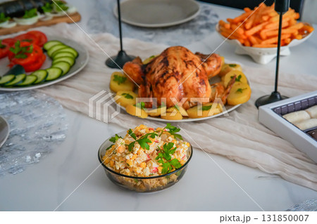 Close-up side view of a festive holiday table featuring roasted chicken, crispy fries, and fresh vegetables. Cozy Christmas, Thanksgiving, or New Year family celebration with colorful and appetizing 131850007
