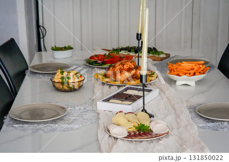 Horizontal view of a festive holiday table fully set with roasted chicken, fresh salads, mandarins, and assorted sweets. Cozy Christmas, Thanksgiving, or New Year family celebration with colorful and Horizontal view of a festive holiday table fully set with roasted chicken, fresh salads, mandarins, and assorted sweets. Cozy Christmas, Thanksgiving, or New Year family celebration with colorful and 131850022