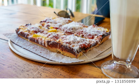 Delicious square pizza topped with cheese and herbs served on a wooden table, accompanied by a refreshing beverage, showcasing culinary delight 131850899