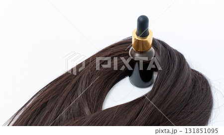 Hair serum bottle placed on smooth surface beside long, shiny dark hair strands, showcasing hair care product and beauty essentials Hair serum bottle placed on smooth surface beside long, shiny dark hair strands, showcasing hair care product and beauty essentials 131851095
