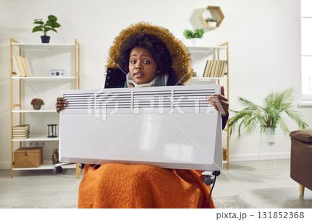 African American young woman in winter jacket holding heater 131852368