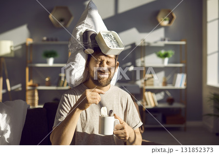 Young man with a pillow and an alarm clock drinks tea as he can't wake up in the morning Young man with a pillow and an alarm clock drinks tea as he can't wake up in the morning 131852373