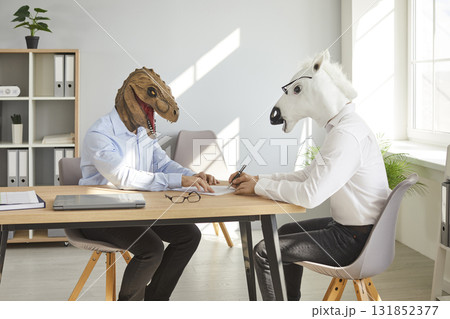 Two funny business men wearing animal masks sitting at their workplace and signing a contract. 131852377
