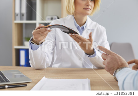 Young woman doctor gives comfortable orthotic medical shoe insole to senior man patient Young woman doctor gives comfortable orthotic medical shoe insole to senior man patient 131852381