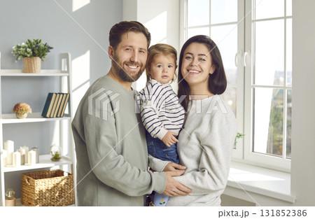 Portrait of young man and wife holding their cute little daughter in their arms together. Portrait of young man and wife holding their cute little daughter in their arms together. 131852386