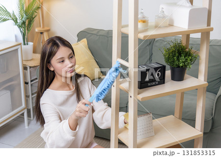 Young woman cleaning home, dusting room shelf, active teen cleaner maintains house cleanliness, busy doing household cleanup work, diligent person keeps modern living space tidy. Young woman cleaning home, dusting room shelf, active teen cleaner maintains house cleanliness, busy doing household cleanup work, diligent person keeps modern living space tidy. 131853315