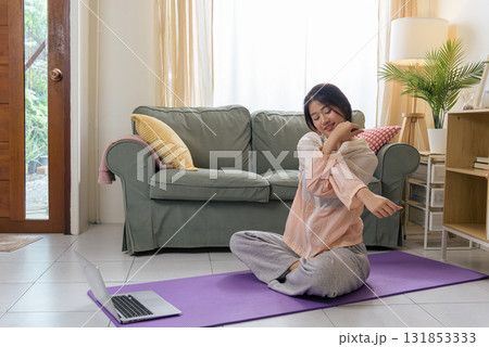 Healthy lifestyle woman exercises yoga for physical health, teen workout at home with sport, young Asian woman stretches arm on purple mat watching online fitness on laptop in bright room. Healthy lifestyle woman exercises yoga for physical health, teen workout at home with sport, young Asian woman stretches arm on purple mat watching online fitness on laptop in bright room. 131853333