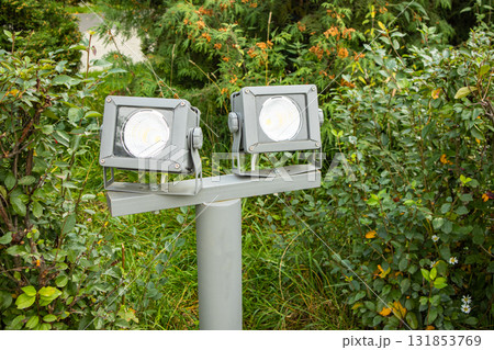 Two LED floodlights on a garden post, gray metal among green foliage 131853769