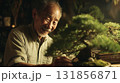 elderly man smiles while tending to bonsai tree in serene setting, showcasing his passion for gardening and nature. warm atmosphere highlights his kind demeanor and dedication 131856871