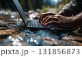 person is typing quickly on waterproof laptop near river, surrounded by nature. scene captures essence of working outdoors, showcasing beauty of technology and nature together 131856873